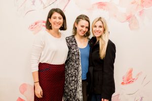 three women posing in front of floral wall at get fabulous event